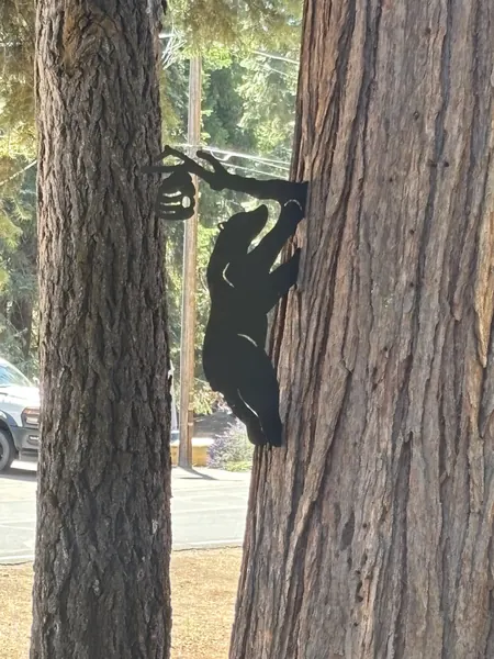 Black steel bear silhouette climbing a tree trunk and reaching for a honey pot on a branch