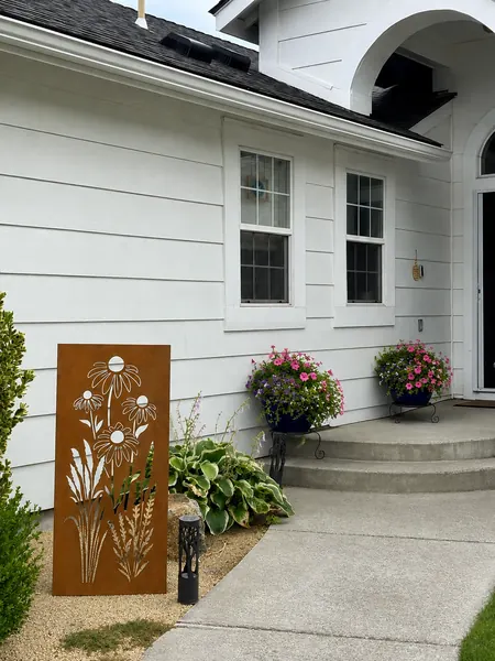 Tall rusted-steel garden panel with a daisy and wildflower cutout standing beside a house entry